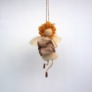 May include: A felt angel ornament with a halo, orange hair, and a brown paper wing. The angel is holding a brown paper scroll.