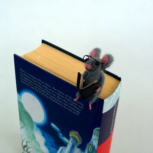 A gray felt mouse wearing glasses and holding a book is perched on top of a Harry Potter book. Detailed view of miniature felt mouse bookmark, handcrafted from natural wool, gift idea for readers