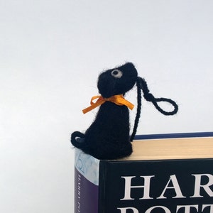 K&ouml;nnte beinhalten: Schwarzer Filz-Lesezeichen in Form eines Hundes mit orangefarbenem Band, das auf einem Buch mit dem Titel "Harry Potter" liegt