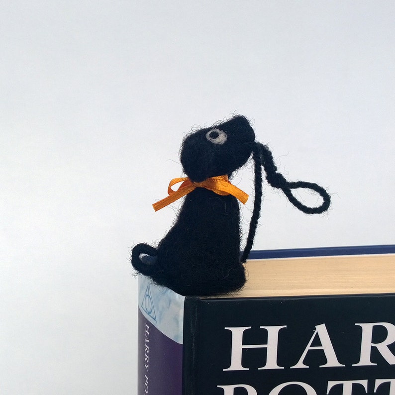 K&ouml;nnte beinhalten: Schwarzer Filz-Lesezeichen in Form eines Hundes mit orangefarbenem Band, das auf einem Buch mit dem Titel "Harry Potter" liegt