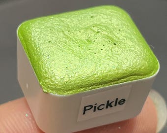 May include: A small, square, green watercolor pan with a white label that says "Pickle".