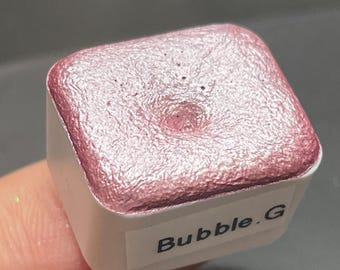 May include: A small, square container of pink metallic paint with the label "Bubble. G" on the front.
