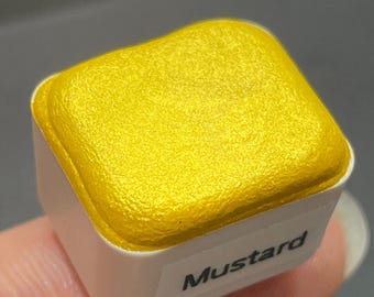 May include: A small, square container of yellow paint with a metallic sheen. The container is labeled "Mustard".