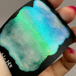 May include: A close-up of a shimmery, iridescent teal and green paint sample on a black card. The paint has a metallic sheen and a textured finish. The card is labeled "No. 145".