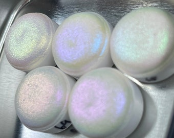 May include: Five small round containers with iridescent white paint inside. The containers are arranged in a semi-circle on a silver surface.