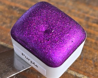 May include: A square pan of purple watercolor paint with a shimmery finish. The pan is labeled "Purple".