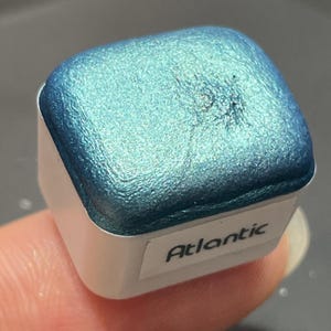 May include: A small, square container of teal blue metallic paint with the word "Atlantic" printed on the label.