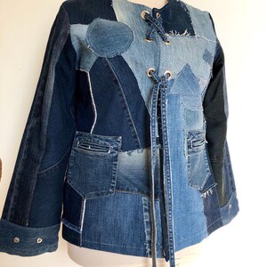 Puede incluir: Chaqueta vaquera patchwork en varios tonos de azul. La chaqueta presenta un diseño único con múltiples parches de mezclilla, bolsillos y un cierre con cordones. Las mangas son largas y la chaqueta tiene un cuello redondo. La chaqueta se exhibe en un maniquí.