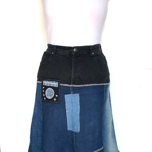 May include: A denim skirt with a black waistband and a patchwork design. The skirt features a flared silhouette with various shades of blue denim and decorative patches. The skirt is displayed on a mannequin with a white tube top.