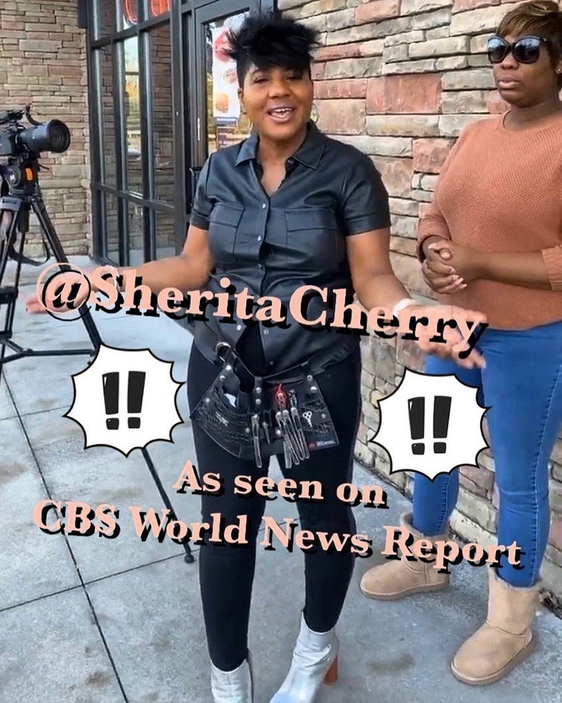 May include: A woman wearing a black leather shirt and black pants with a tool belt. She is standing in front of a brick wall with a camera and tripod in the background. The text "@SheritaCherry" and "As seen on CBS World News Report" is visible in the image.