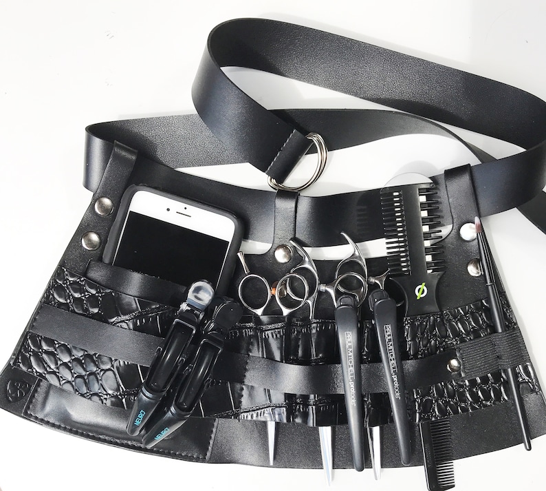 May include: Black leather barber's belt with multiple pockets and loops for holding tools. The belt has a crocodile-embossed pattern and includes a comb, scissors, and a razor.