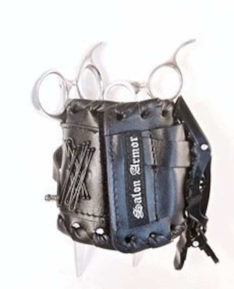 Puede incluir: Porta tijeras de cuero negro con dise&ntilde;o de guante de b&eacute;isbol. El porta tijeras tiene una correa con hebilla y el texto "Salon Armor" est&aacute; impreso en el lateral.