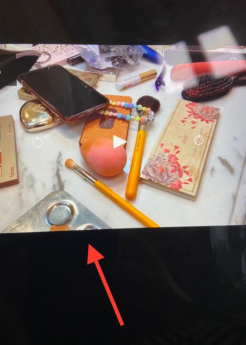 Puede incluir: Primer plano de un tocador de maquillaje con varios art&iacute;culos, incluyendo un tel&eacute;fono inteligente negro, un estuche dorado, una esponja de maquillaje rosa, una brocha de maquillaje amarilla, una paleta de maquillaje plateada y una paleta de maquillaje con estampado floral con la palabra "Jouer" impresa en ella.