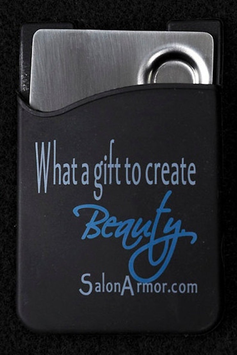 Puede incluir: Una funda de silicona negra con un inserto de metal plateado. La funda tiene el texto "What a gift to create Beauty SalonArmor.com" impreso en ella.