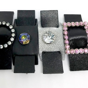 Puede incluir: Cuatro correas de cuero negro con diferentes hebillas decorativas. Las hebillas est&aacute;n adornadas con diamantes de imitaci&oacute;n transparentes, iridiscentes y rosas.