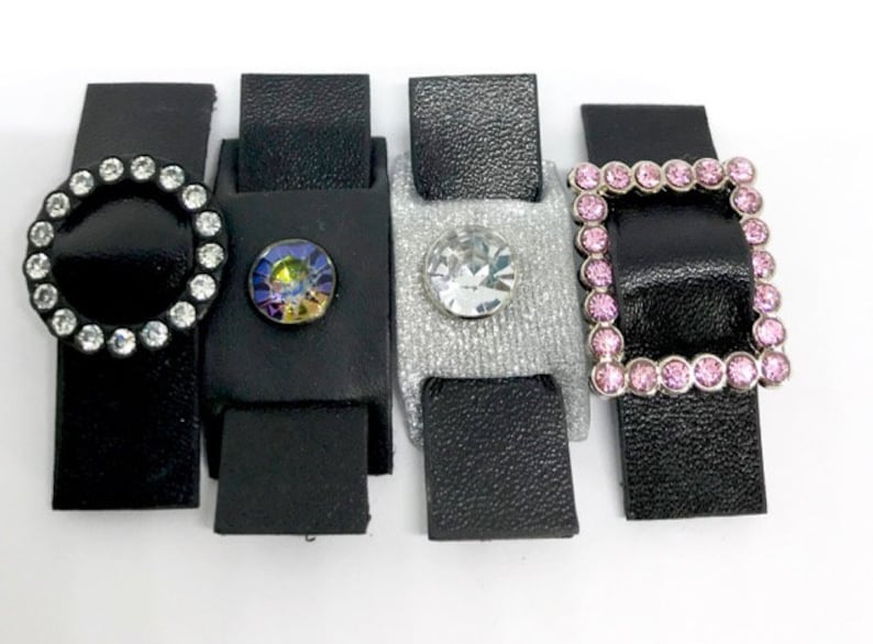 Puede incluir: Cuatro correas de cuero negro con diferentes hebillas decorativas. Las hebillas est&aacute;n adornadas con diamantes de imitaci&oacute;n transparentes, iridiscentes y rosas.