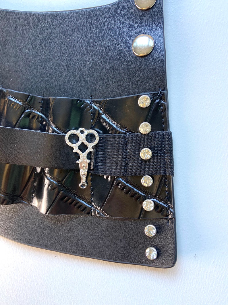 May include: Black leather belt with a silver key charm and rhinestones. The belt has a black elastic band and a crocodile-embossed design.