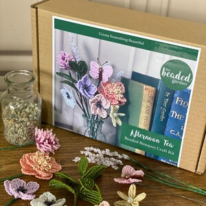 May include: A craft kit for making beaded bouquets, with various colourful beaded flowers and a butterfly. The kit includes a box with the text "Afternoon Tea Beaded Bouquet Craft Kit" and a glass jar with small stones.