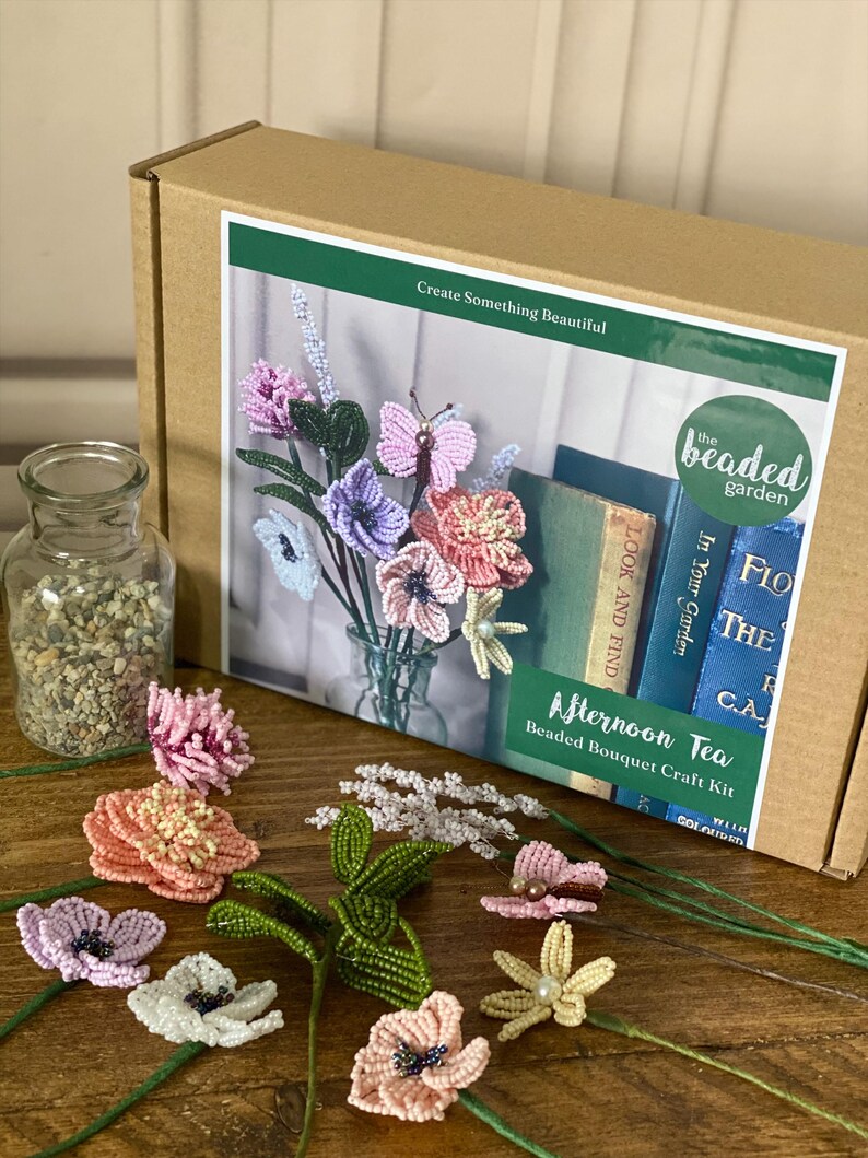 May include: A craft kit for making beaded bouquets, with various colourful beaded flowers and a butterfly. The kit includes a box with the text "Afternoon Tea Beaded Bouquet Craft Kit" and a glass jar with small stones.
