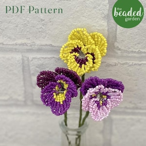 Może przedstawiać: Trzy łodygi kwiatów z koralików w szklanym wazonie. Kwiaty są fioletowe, żółte i różowe. Kwiaty są wykonane z małych koralików i mają realistyczny wygląd. Tekst "PDF Pattern" i "the beaded garden" jest widoczny na zdjęciu.