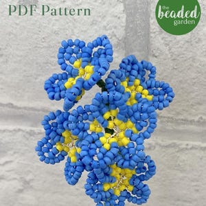 Puede incluir: Un arreglo floral de cuentas con cuentas azules y amarillas. La flor está hecha con pequeñas cuentas y tiene un diseño detallado. El texto "PDF Pattern" está en la esquina superior izquierda, y un círculo verde con "the beaded garden" está en la esquina superior derecha.