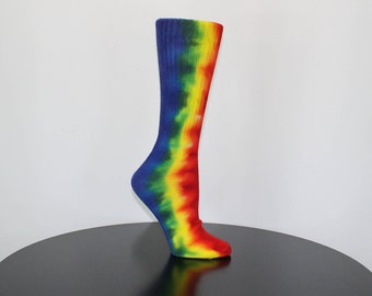 May include: A pair of rainbow tie-dye socks with a blue, yellow, red, and green color scheme. The socks are on a black surface.
