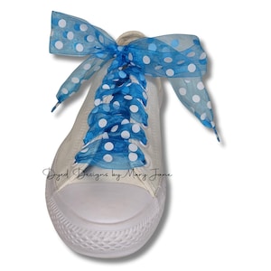 May include: Cream canvas trainer with blue polka dot ribbon laces. The laces are tied in a bow. The text "Dyed Designs by Mary Jane" is printed on the side of the shoe.
