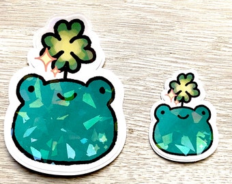 May include: Two green frog stickers with a four-leaf clover on top. The frogs are made of a sparkly, iridescent material.