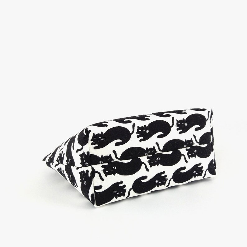 Puede incluir: Un bolso tote rectangular con un patr&oacute;n repetido de gatos negros sobre un fondo blanco. Los gatos est&aacute;n en varias poses, creando un dise&ntilde;o l&uacute;dico. El bolso est&aacute; hecho de una tela resistente.