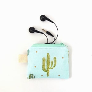 Puede incluir: Peque&ntilde;o estuche con cremallera azul claro con dise&ntilde;o de cactus y lunares dorados. Auriculares negros y un conector para auriculares sobresalen de la parte superior. Un lazo de tela beige est&aacute; unido al lateral. El estuche est&aacute; dise&ntilde;ado para guardar objetos peque&ntilde;os.