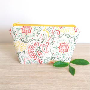 Puede incluir: Un peque&ntilde;o neceser rectangular con cremallera amarilla. La bolsa presenta un fondo blanco con un colorido estampado de cachemira en rojo, verde, amarillo y rosa. Est&aacute; sobre una superficie de madera.