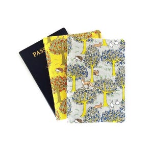 May include: Three passport holders with nature-themed patterns. One is navy blue with the word "PASS" in gold. The other two feature colorful tree and animal designs, including foxes, hedgehogs, and rabbits, on yellow and grey backgrounds.