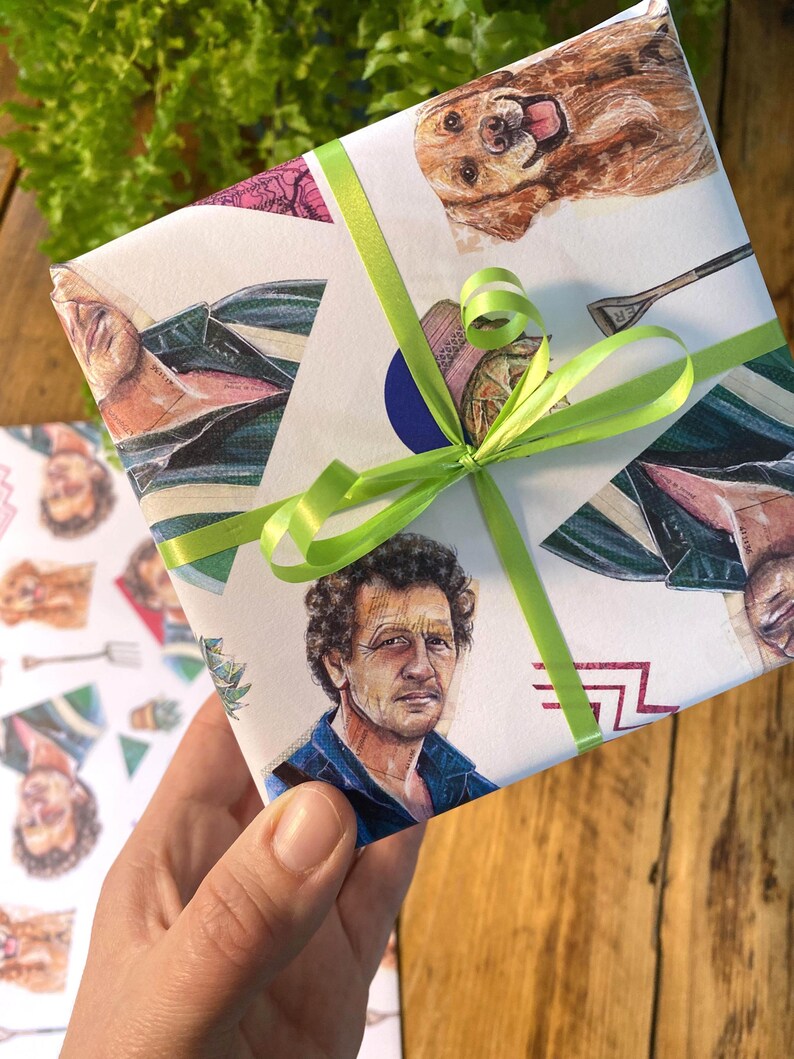May include: Gift-wrapped present with a white background featuring illustrations of a man, a dog, and other objects. The gift is tied with a bright green ribbon. The wrapping paper has a collage-like design with various images.