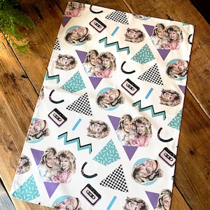 May include: A white tea towel with a repeating pattern of a couple, cassette tapes, and geometric shapes in shades of blue, purple, black, and white.