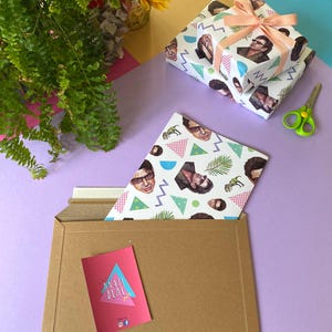 May include: Two gift-wrapped presents with a peach ribbon, patterned with faces, geometric shapes, and dinosaurs. A brown envelope contains a card with "MAIL DEAL" and a matching patterned sheet. Green scissors and flowers are also visible.