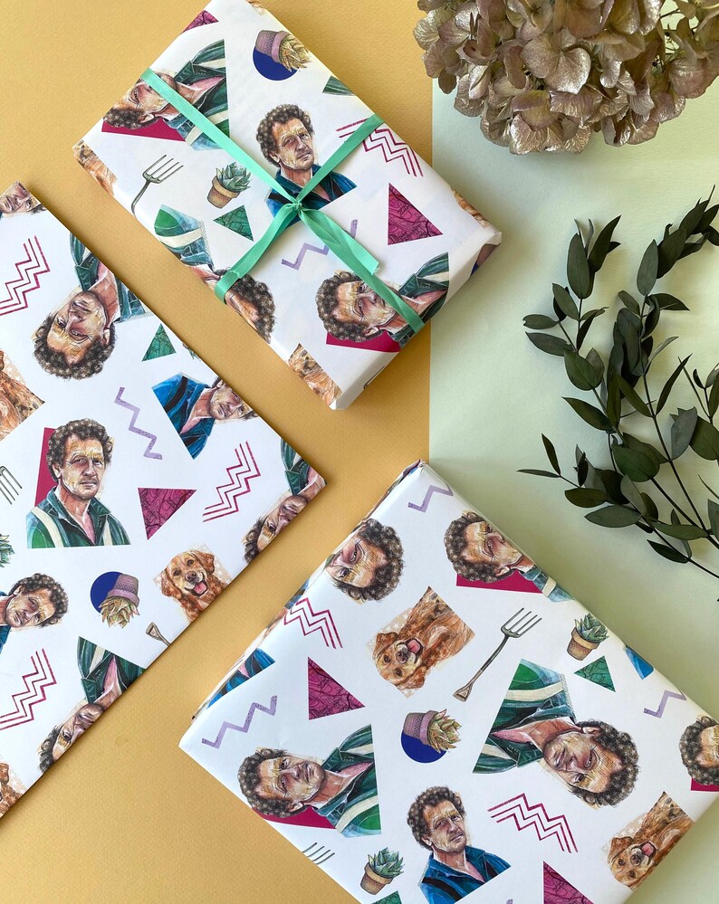 May include: White wrapping paper with a repeating pattern of a man's portrait, a golden retriever, a gardening fork, and geometric shapes. A gift is wrapped with a light green ribbon. The background is a mix of yellow and light green.