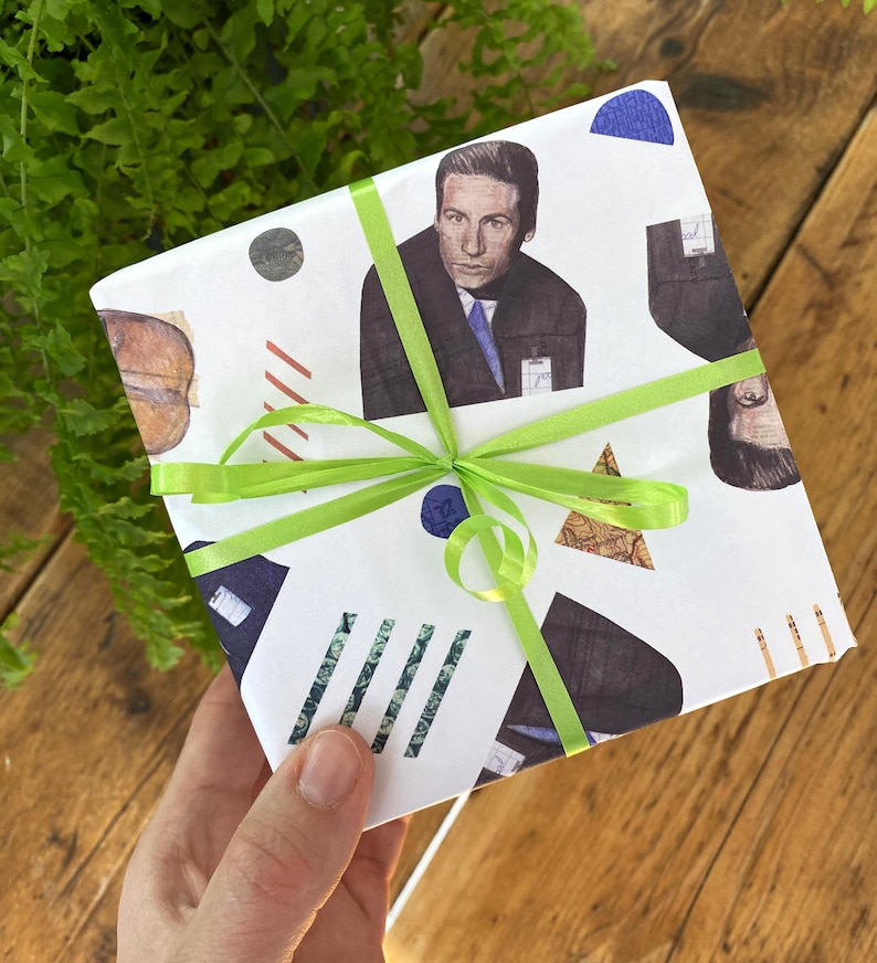 May include: White gift wrap with a green ribbon. The wrap features a repeating pattern of geometric shapes and black and white images of a man in a suit.
