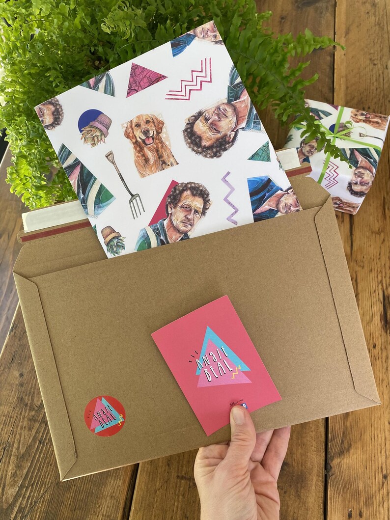 May include: A brown kraft paper envelope with a pink card and sticker featuring the text "ANGIE BEAL" in a retro design. Inside, a patterned card with illustrations of a dog, a man, and geometric shapes. A wrapped gift is also visible.