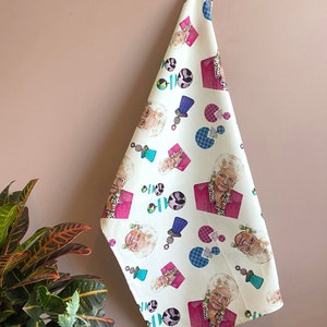 May include: A white kitchen towel with a colourful pattern featuring a woman's face, geometric shapes, and polka dots.