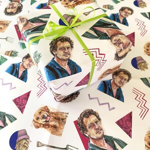 May include: A wrapped gift on a white background, featuring a repeating pattern of a man's portrait, a dog, and other graphics. The gift is tied with a bright green ribbon. The wrapping paper has a retro, artistic design.