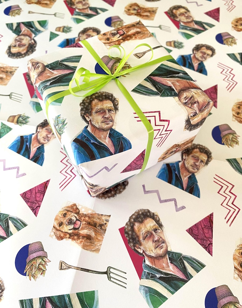 May include: A wrapped gift on a white background, featuring a repeating pattern of a man's portrait, a dog, and other graphics. The gift is tied with a bright green ribbon. The wrapping paper has a retro, artistic design.