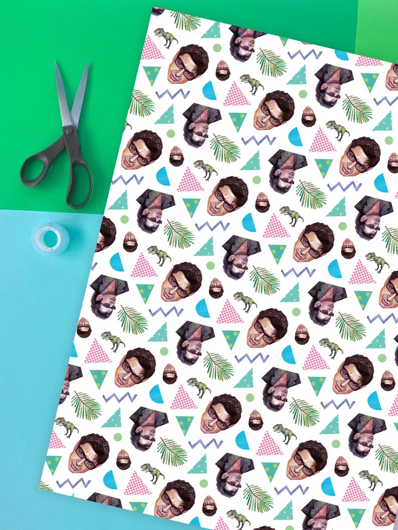 May include: White wrapping paper featuring a repeating pattern of a man's face, dinosaurs, and geometric shapes in blue, pink, and green. Scissors and tape are on a green and blue background.