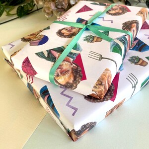 May include: Two gift-wrapped packages with white paper featuring a repeating pattern of illustrated faces, triangles, and other shapes. A light green ribbon is tied around the top package. The packages are stacked on top of each other.