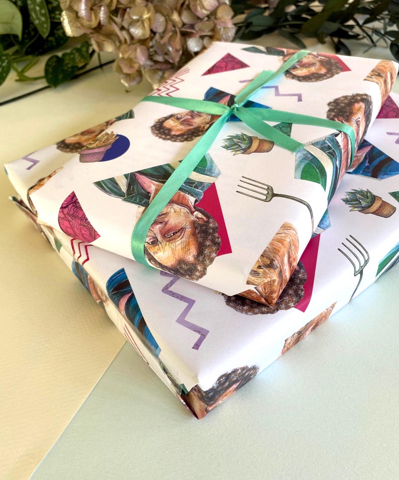 May include: Two gift-wrapped packages with white paper featuring a repeating pattern of illustrated faces, triangles, and other shapes. A light green ribbon is tied around the top package. The packages are stacked on top of each other.