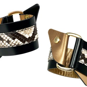 May include: Two black leather bracelets with gold buckles and a snakeskin pattern.