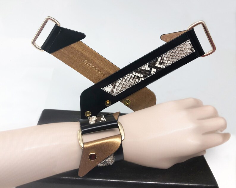 May include: A black and gold leather bracelet with a snakeskin pattern. The bracelet has a buckle closure and is adjustable.