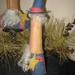 May include: Two handmade rag dolls dressed in red, white, and blue. The doll on the left is wearing a blue hat and the doll on the right is wearing a blue hat with a red band. Both dolls have white yarn hair and are holding a yellow star.