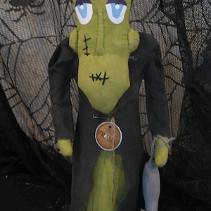 May include: A handmade Frankenstein's monster doll with a green body, black hair and coat, and blue eyes. The doll has stitched details and a tag that reads "Fran". It holds a gray mouse.