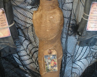 May include: A brown fabric doll with a vintage Halloween postcard attached. The doll is wrapped in fabric and has a stitched face. The postcard shows two children trick-or-treating.