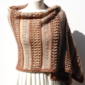 May include: A brown and beige knitted shawl with a striped pattern and a crocheted border. The shawl is draped over a white dress form.